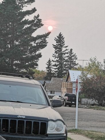 the red sun glaring over the trees as its smokey and hazy outside Hanna, AB